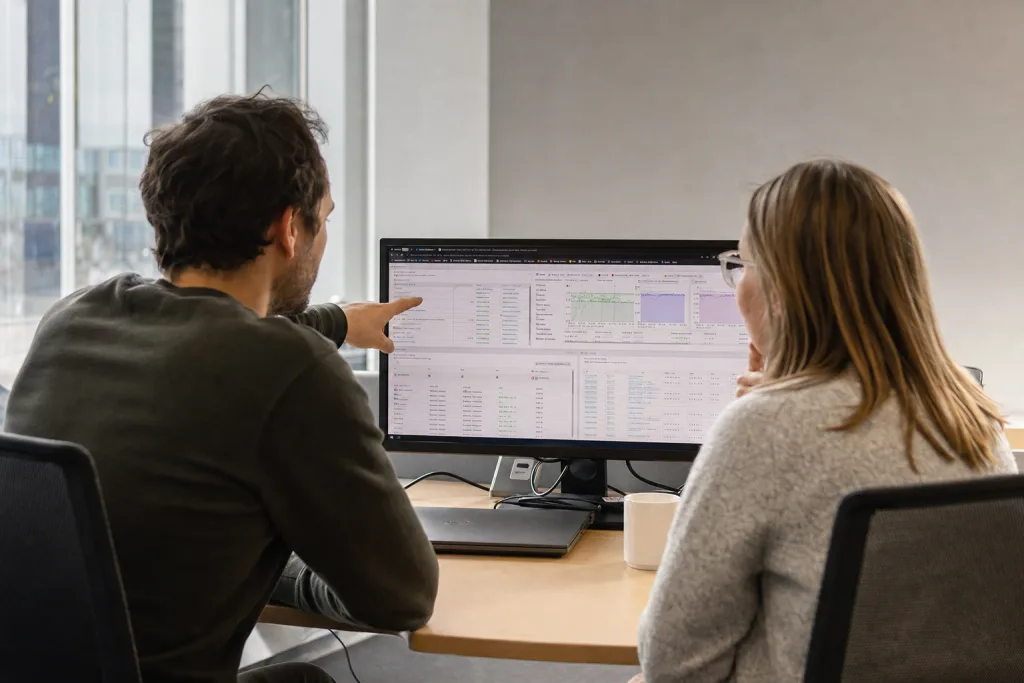 Symbolbild: zwei Personen betrachten gemeinsam ein Monitoring-Dashboard auf einem Bildschirm.